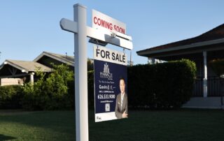 Real estate “for sale” sign with “coming soon” banner in front of a suburban house and yard