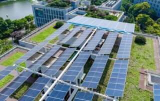 Rooftop solar panels installed above a green roof on a modern office building near a park and water.