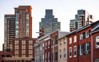 Row houses in front of modern high-rise apartment and office buildings in an urban neighborhood at sunset.