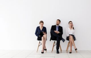 Three business professionals sitting on chairs in a bright minimalist room, waiting for an interview.