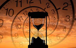 Hourglass silhouette with sand falling in front of spiraling clock faces over an orange sunset sky.