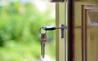Key with a black keychain hanging in a front door lock with a blurred green background