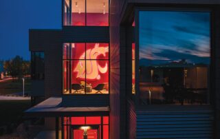 Modern glass building at dusk with a large illuminated cougar logo visible through the windows
