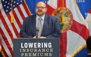 Man speaking at podium about lowering insurance premiums in front of american and florida state flags.
