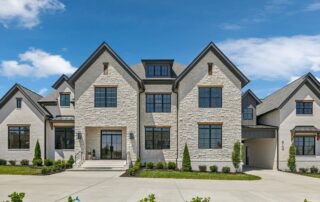 Luxury modern farmhouse style two-story white brick home with black framed windows, dormers, and a wide concrete driveway under a blue sky.
