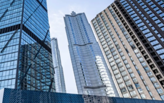 Modern glass skyscrapers and high-rise office buildings viewed from below against a clear blue sky.