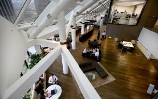 Modern open-plan office atrium with people working and meeting in shared seating areas