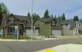 Row of newly built suburban houses with garages along a quiet residential street.