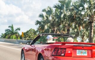 Senior couple driving a red convertible on a sunny highway lined with palm trees