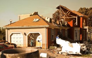 Severely damaged suburban house with collapsed roof and scattered storm debris in the yard