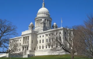 Grand white domed government building on a hill with bare trees under a clear blue sky