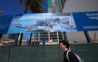 Man walking past a fenced construction site with a large billboard showing a luxury waterfront condo rendering.