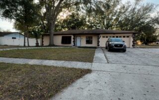 Single-story suburban house with large front yard, concrete driveway, and a black suv parked in front of a two-car garage.